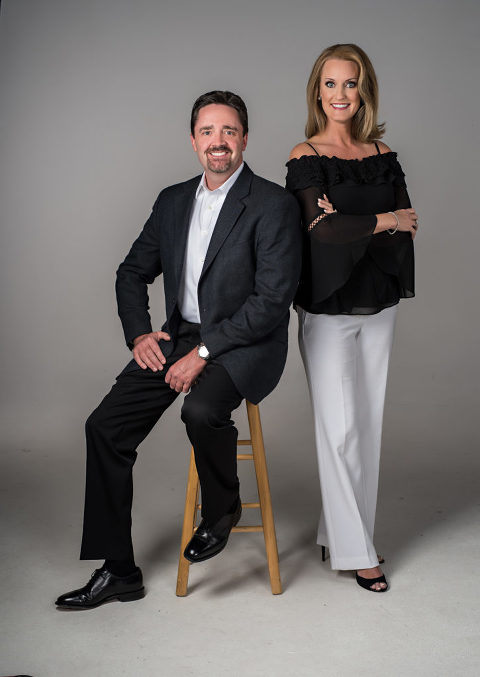 man in black suit sitting on stool on left woman in white dress pants and black blouse standing on right, business portraits, house flippers, atlanta photographer, business photography, commercial photography